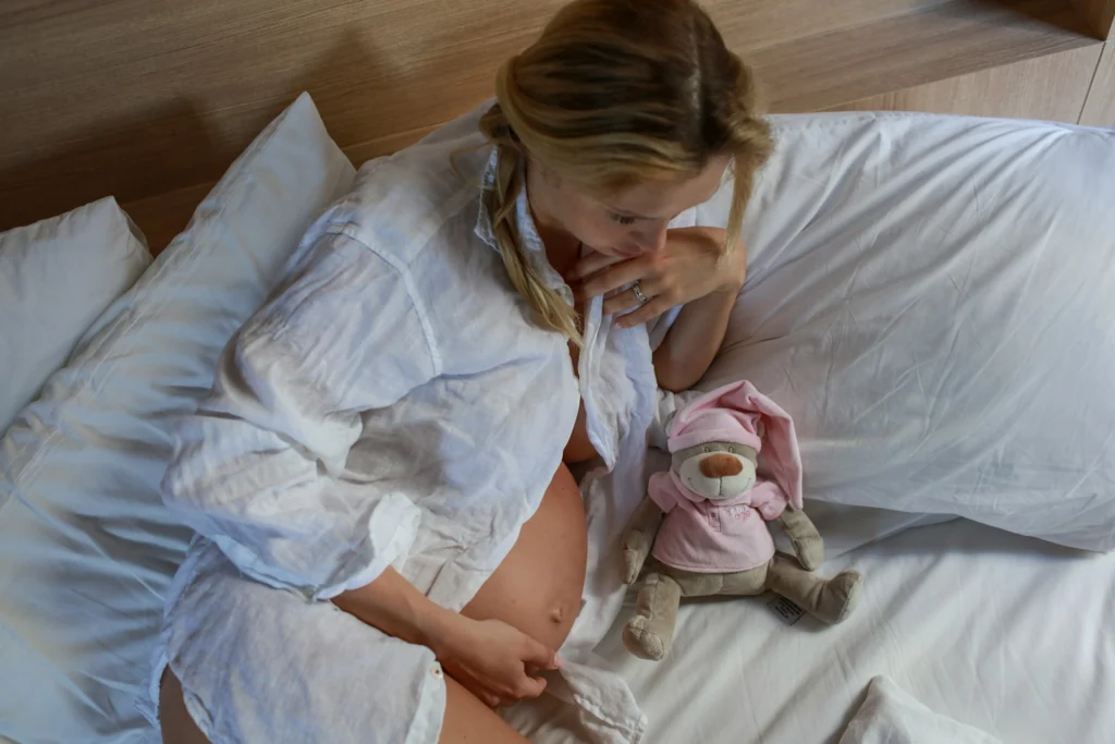 Pregnant woman resting on bed next to stuffed animal