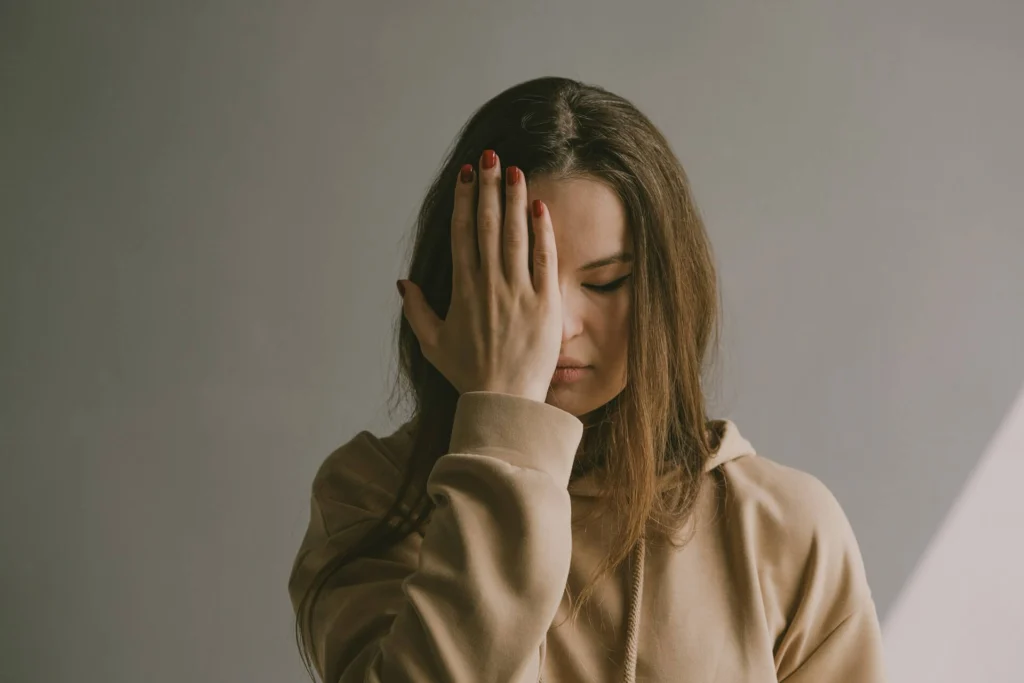 Close-up studio portrait of a woman covering her face with both hands, eyes closed
