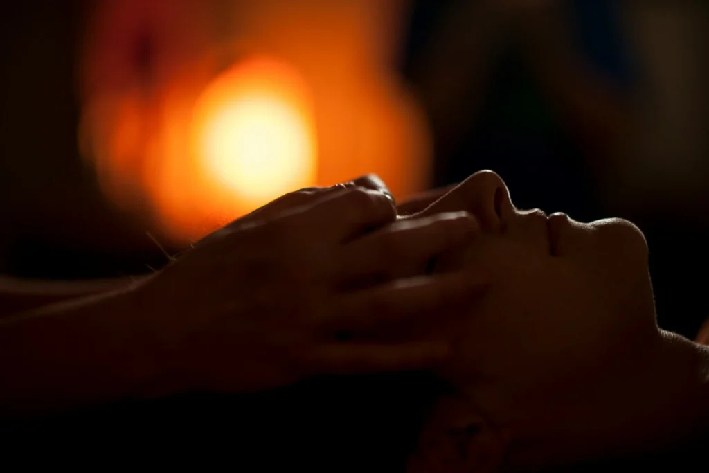 Hands giving a gentle head and face massage in a dimly lit, warm-toned room