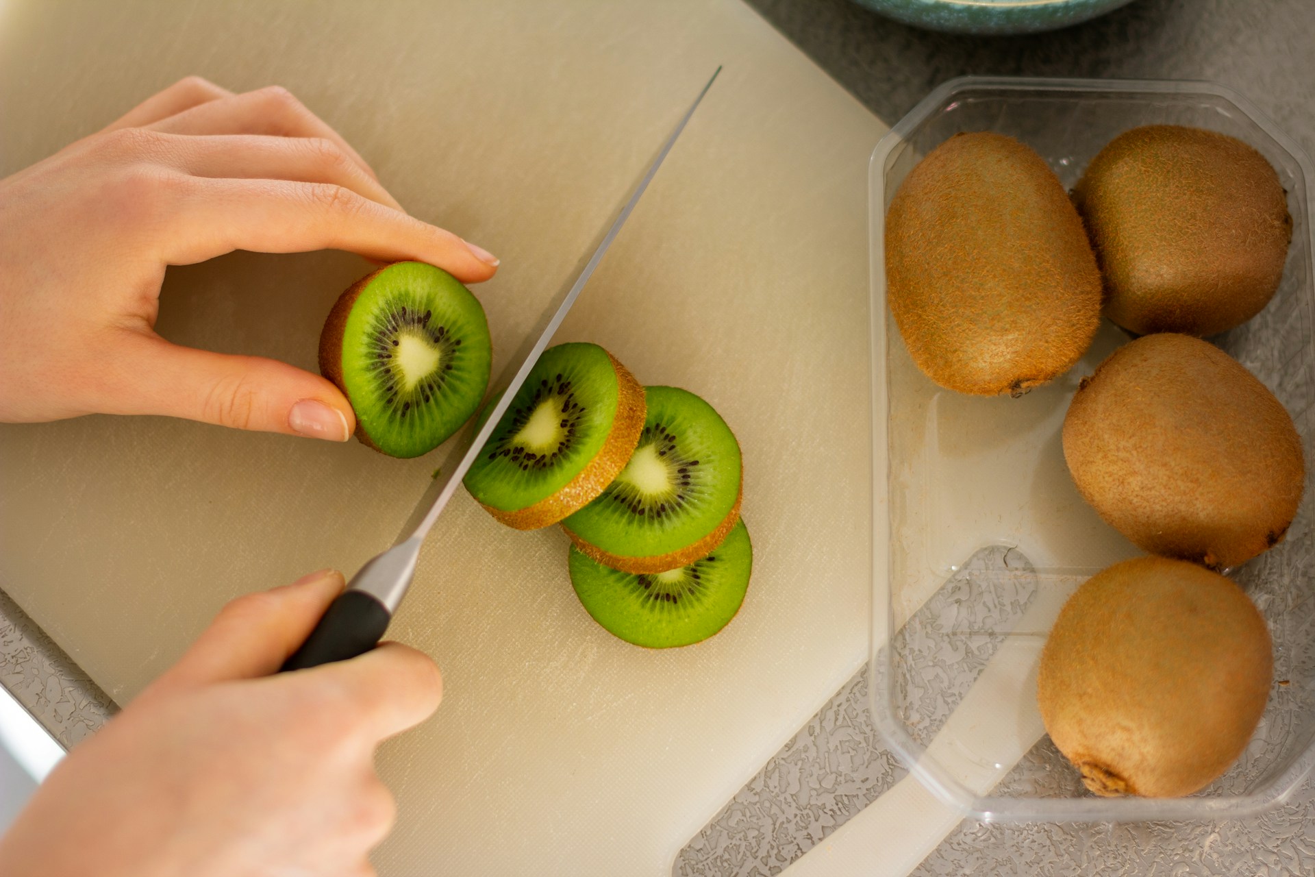 Close-up of fresh kiwi fruit being sliced on a white, plastic cutting board