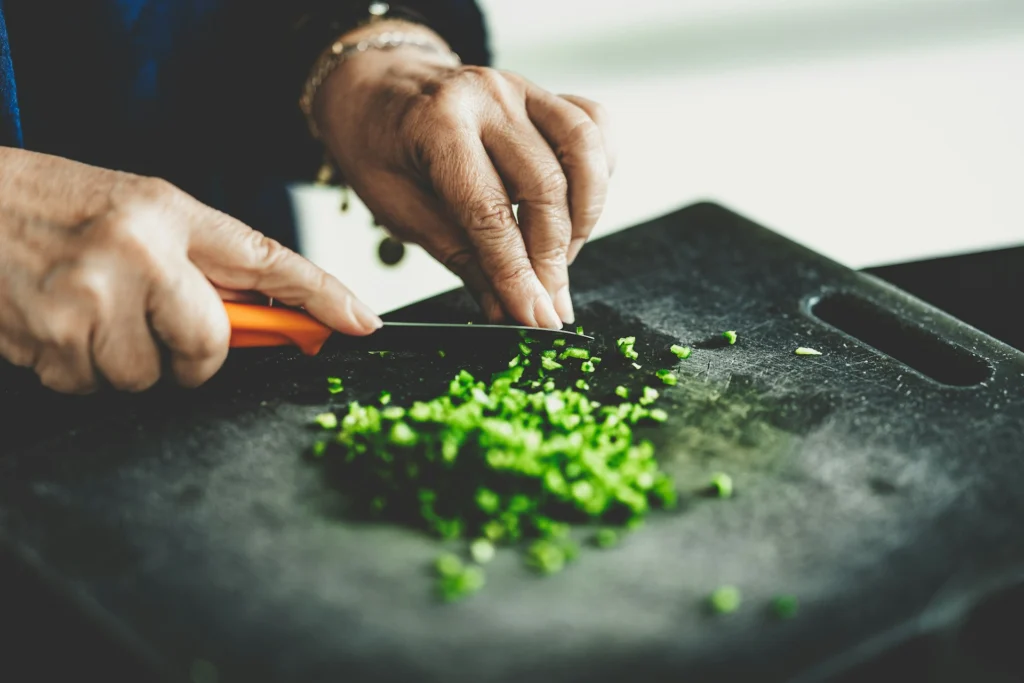Person's hands dicing green vegetables with a knife on a cutting board