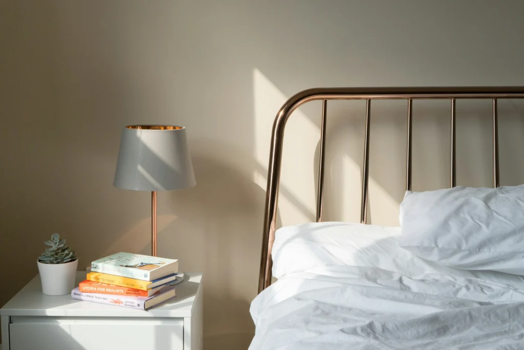 Table lamp on a white nightstand beside a bed in a calm bedroom set up for better sleep