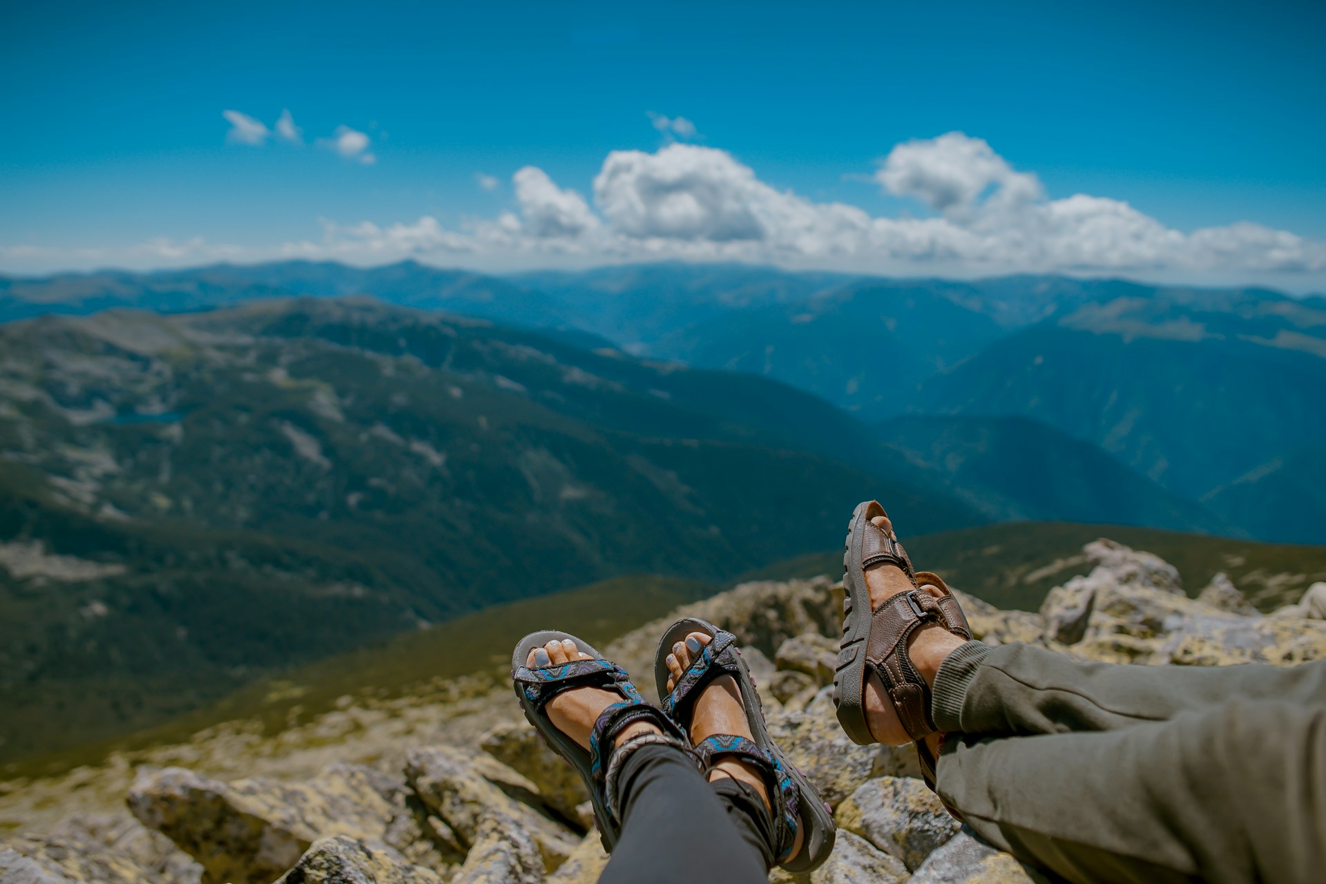 Two people wearing hiking sandals with mountain scenery behind