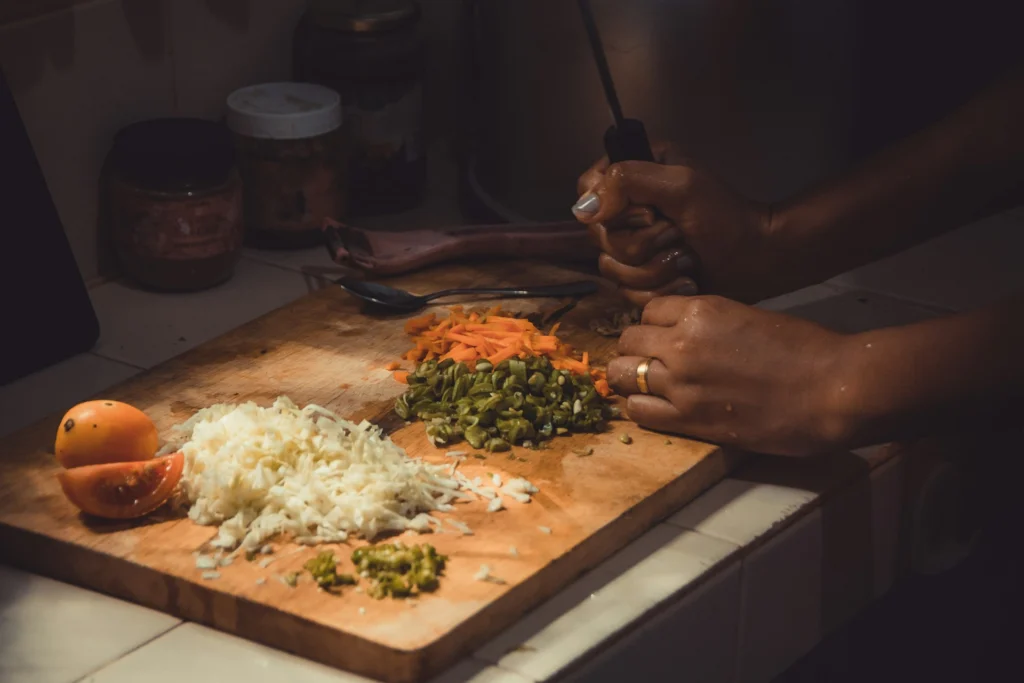 Person cutting vegetables on a wooden board while cooking at home