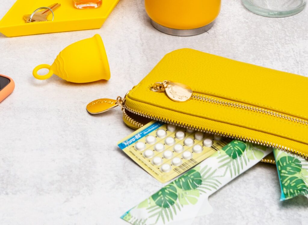 Birth control and tampons falling out of yellow wallet.