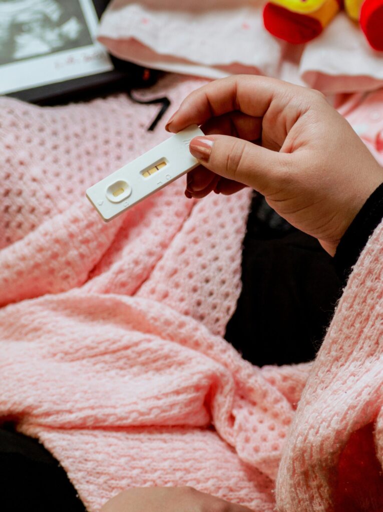 Woman holding positive cassette pregnancy test with ultrasound photo in background.