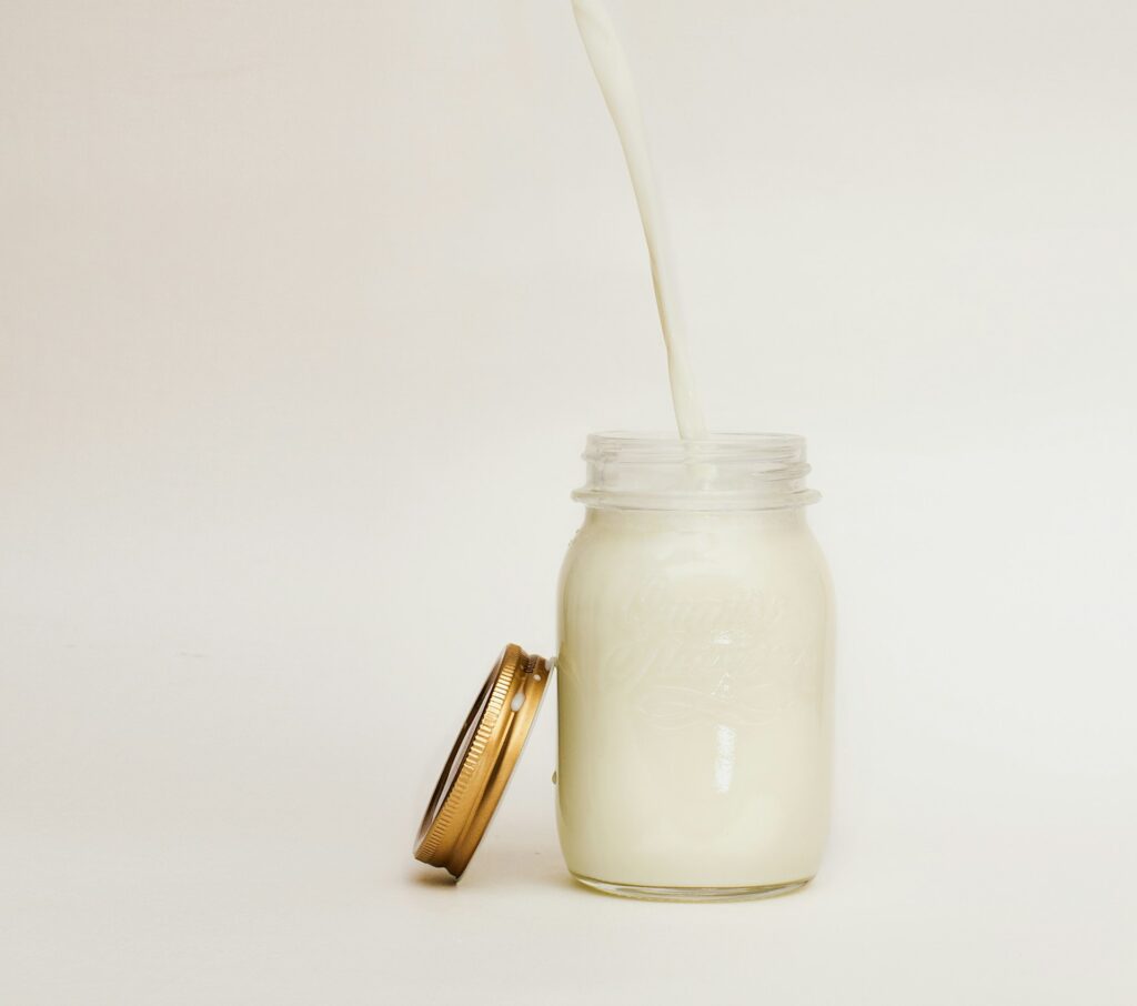 Milk pouring into a mason jar from high above it against a white background.