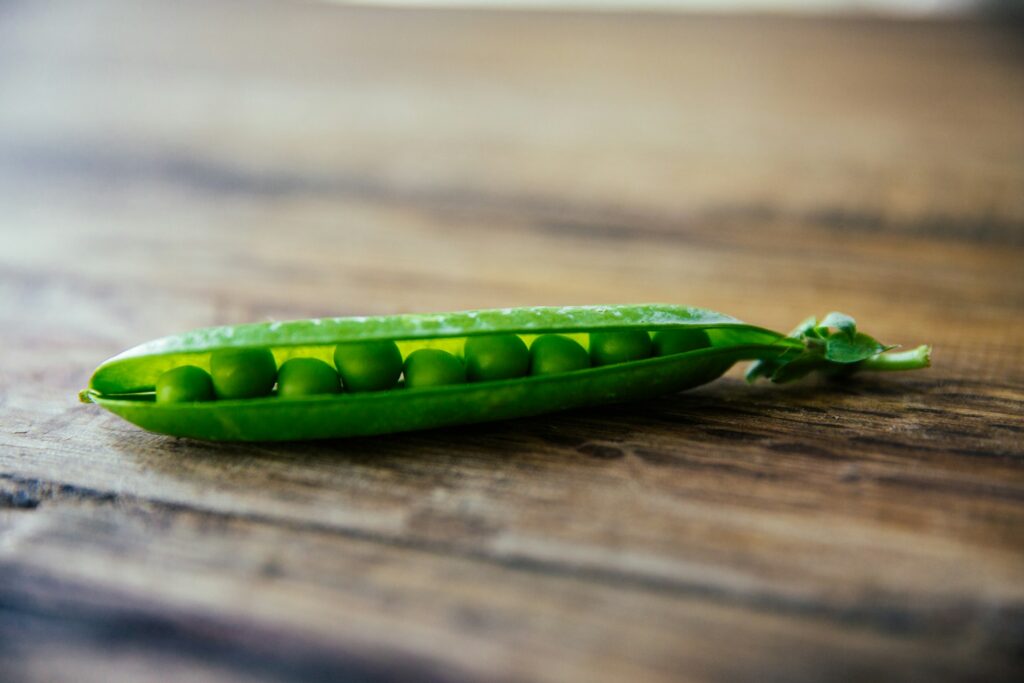 A full pea pod split down the middle sits on a wooden counter.