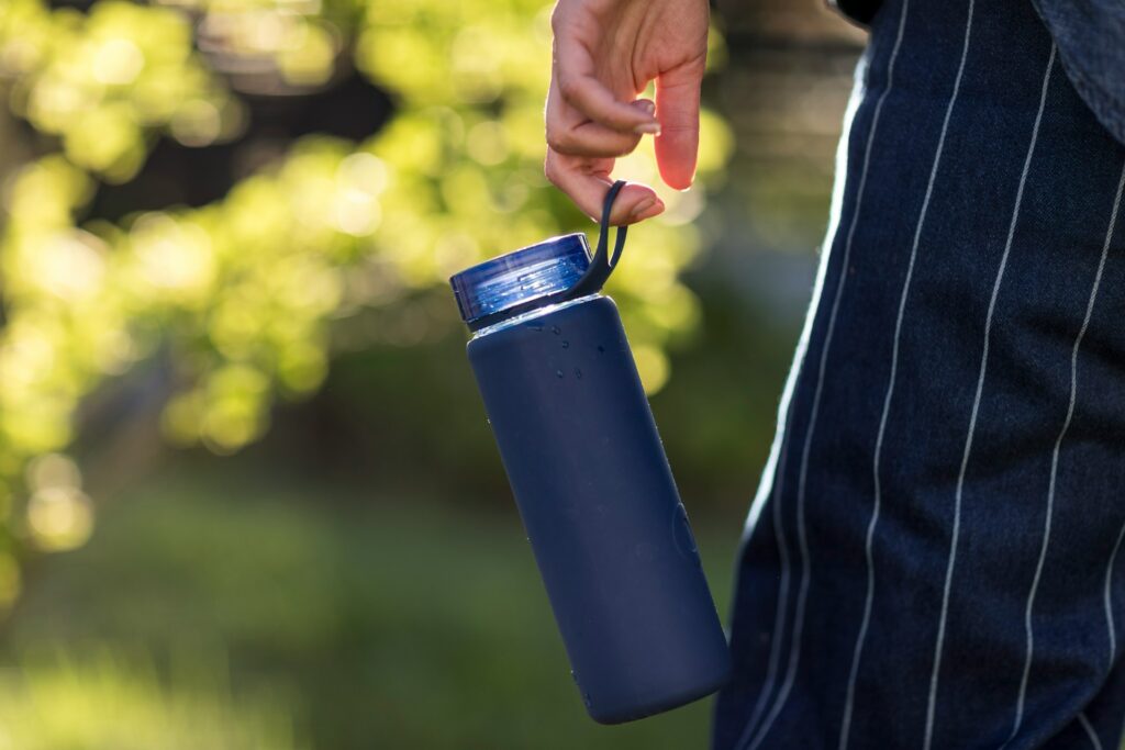 A person in blue linen pants with thin white stripes carries a navy water bottle. It shines against the blurry greenery in the background.