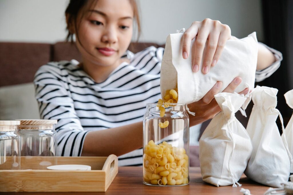 A woman pouring dry noodles into a glass storage container