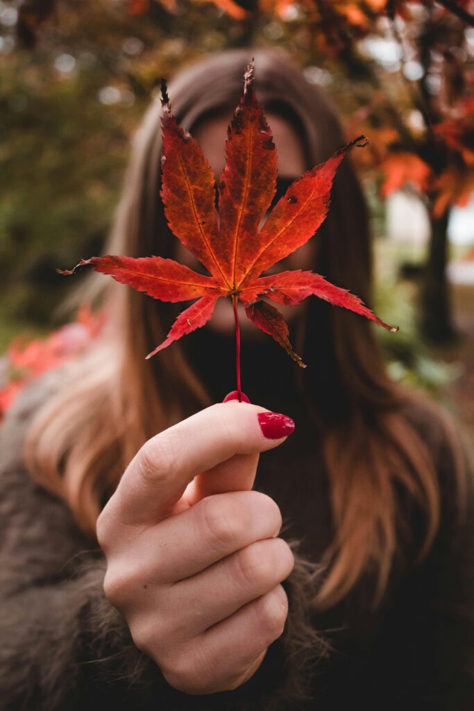 A girl with red nail polish holding a leaf