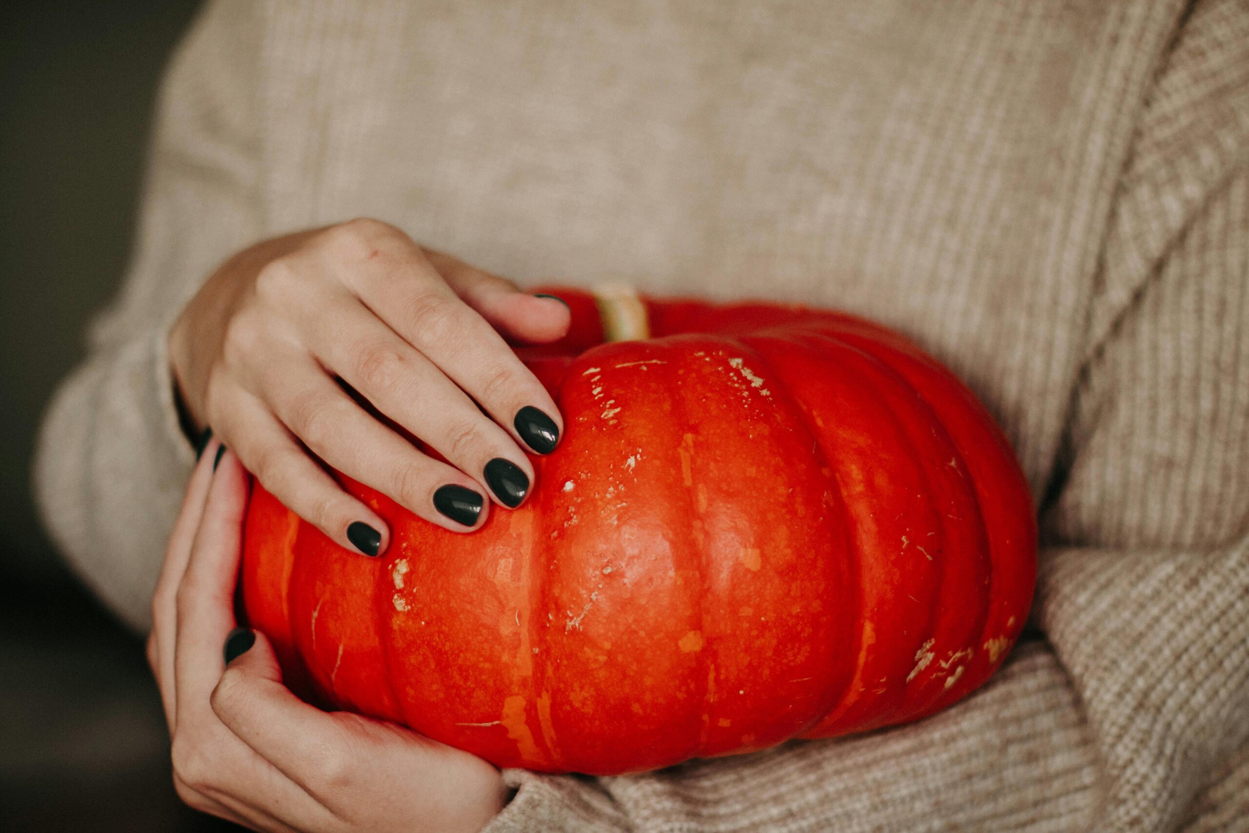 A girl with black nail polish holding an orange pumpkin