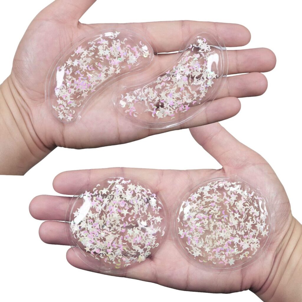 A person holds four cooling gel packs in their hands. Two are circles with clear gel containing sparkly stars and moons. The other two are banana-shaped gel packs containing the same gel and sparkly shapes. They're not frozen yet.