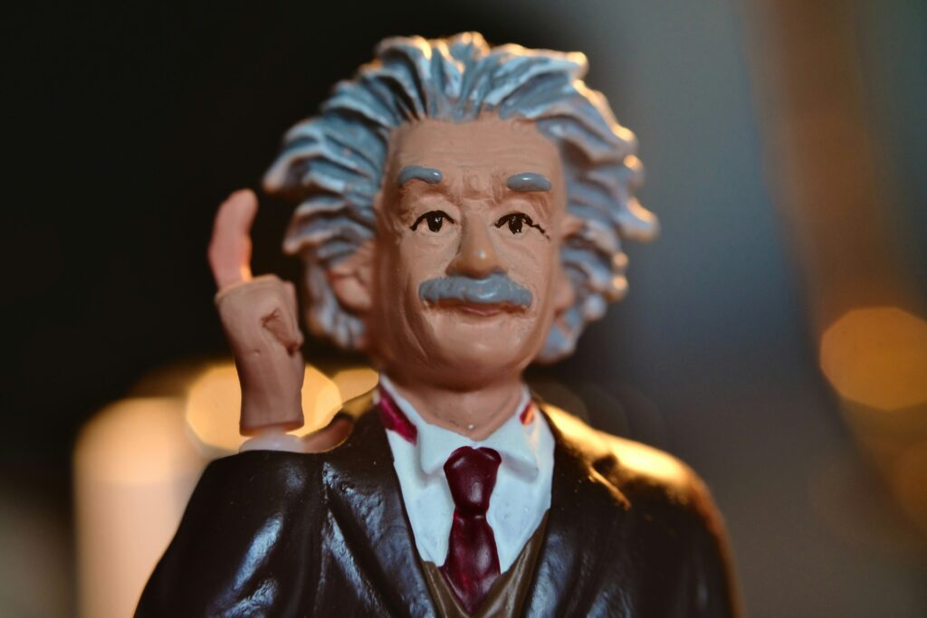 A toy figurine that's slightly aged and resembles Albert Einstein. He holds up a finger to his temple.