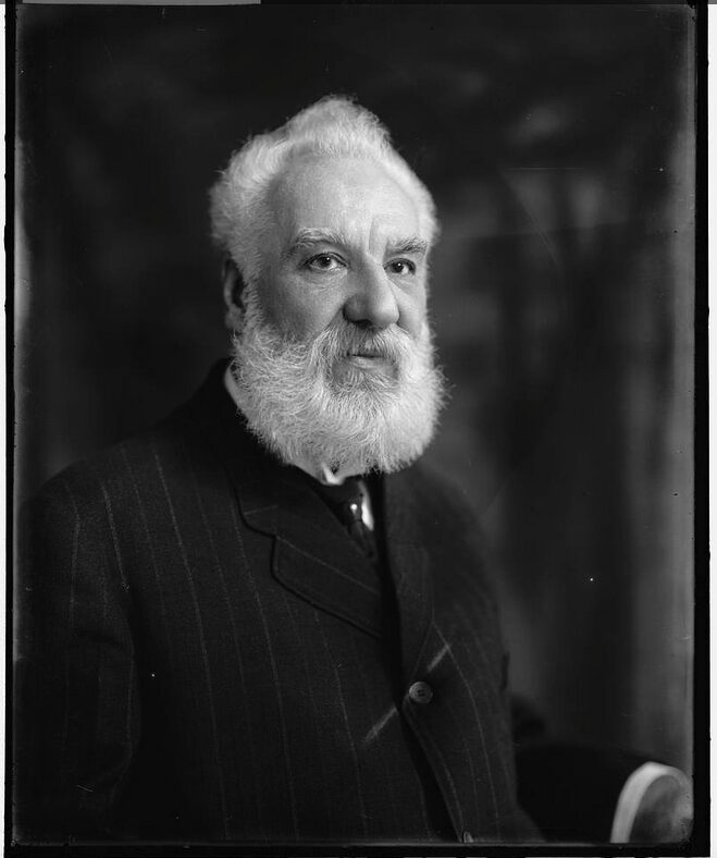 A black and white photo of Alexander Graham Bell in a black suit with thin white stripes.