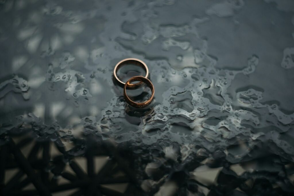 Two brass rings, one with bent edges, sit on a dark glass surface wet with fresh rain water.