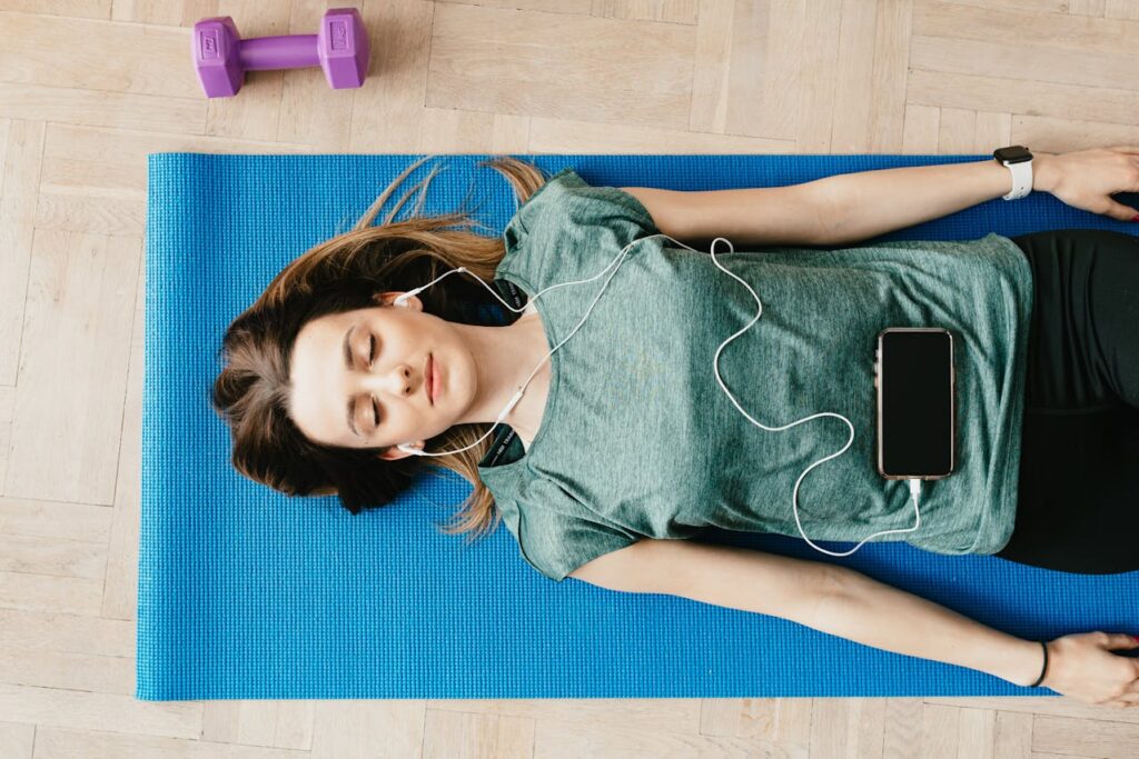 A girl listening to a meditation app with ear buds and laying on a yoga mat 