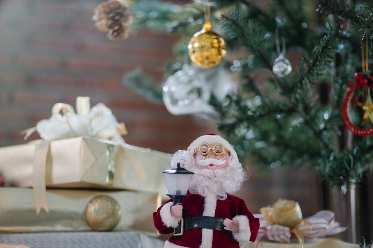 An Santa ornament in the foreground of Christmas presents under a Christmas tree