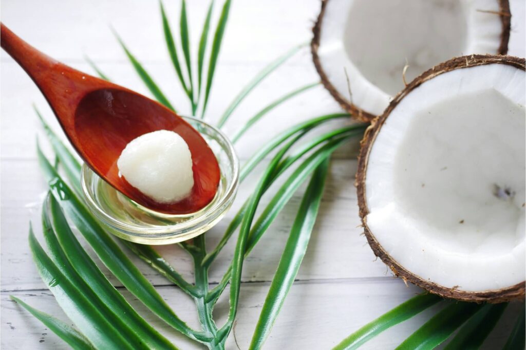 A spoon full of coconut oil next to a halved coconut
