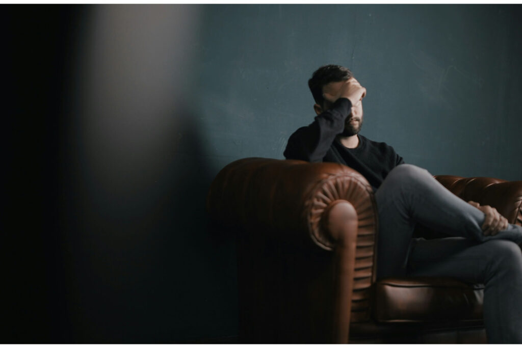 An upset man sitting on a sofa with his head in his hand. 