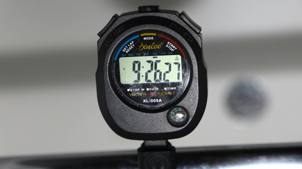 A black stopwatch sits on a stand, reading 9:26:27. It has buttons for lap rests, modes and starting or stopping the device.