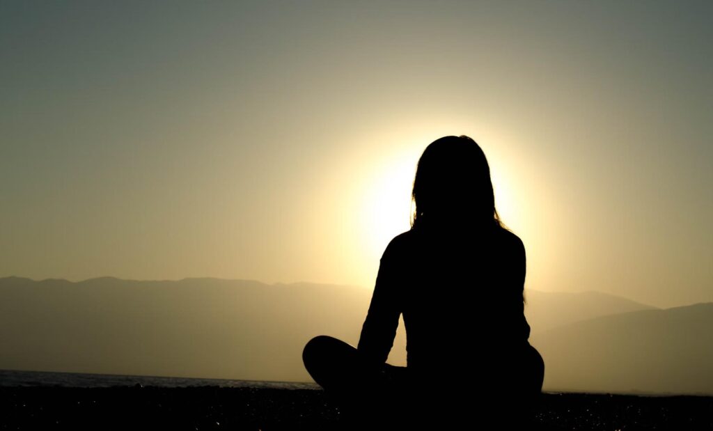 silhouette of a woman sitting and watching the sun