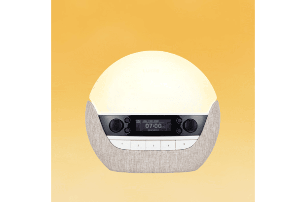 A glowing Lumie Bodyclock Luxe 700FM sunrise alarm clock that shows the time on its front