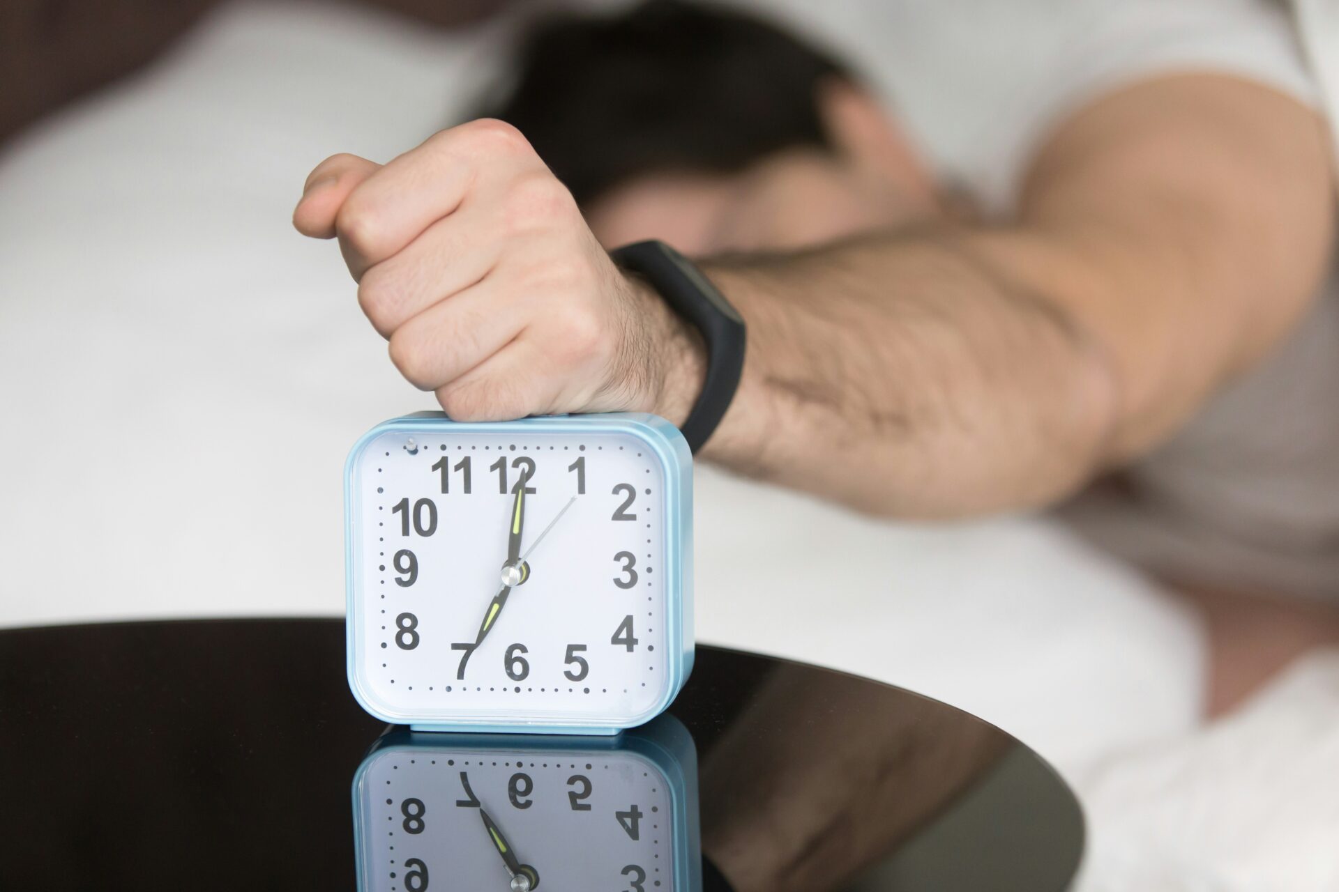 A man turning off an alarm clock in the morning.
