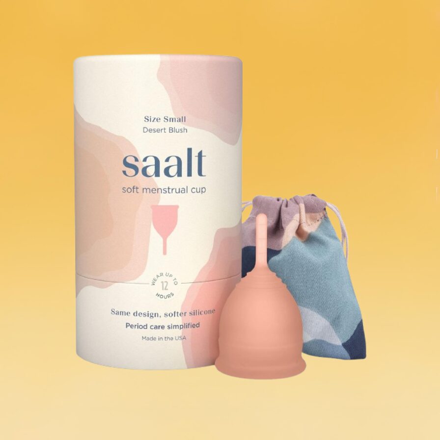 A white and pink container for Saalt's menstrual cup with its storage bag sits against the Body+Mind branded background.