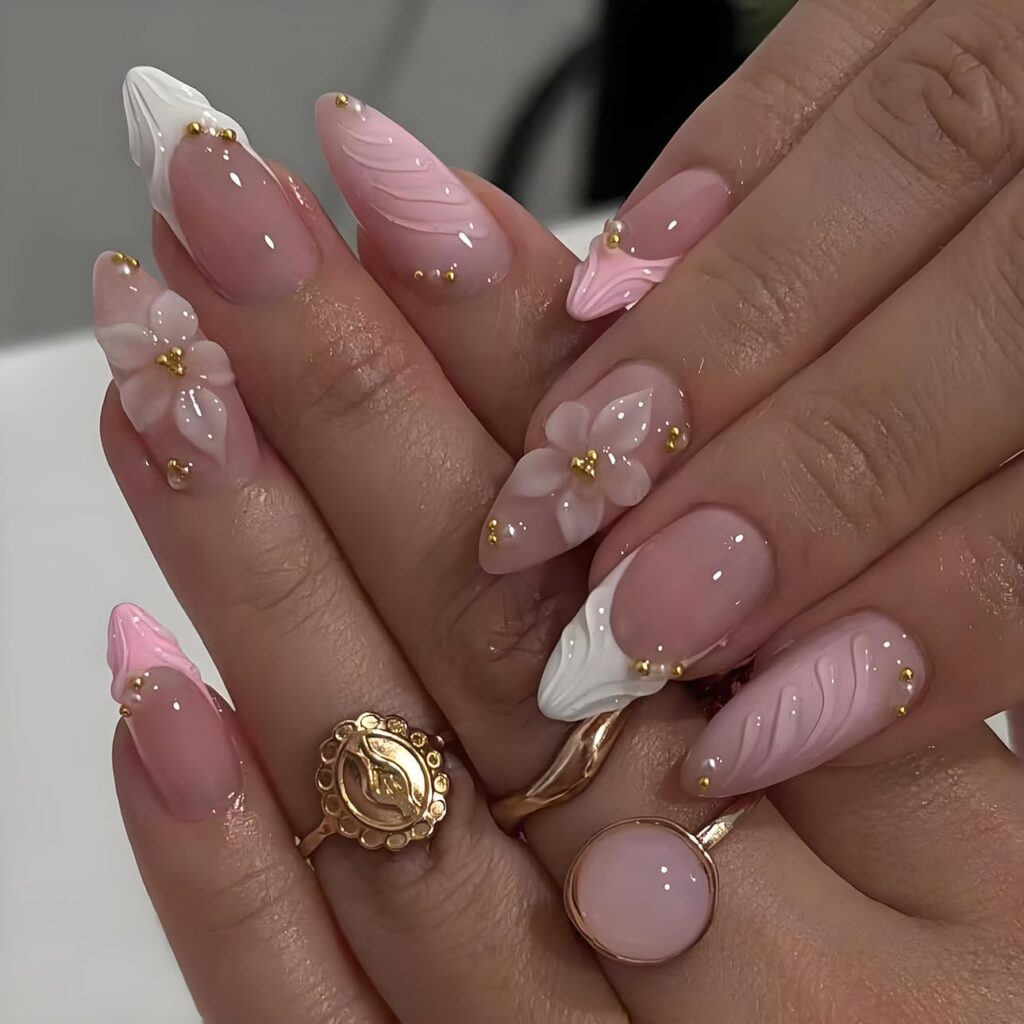 A woman wears pink French tip press-on nails with flower embossments and gold beads.