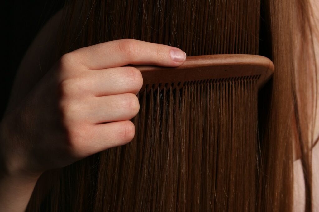 A hand gently combs long, smooth brown hair with a brown, wooden comb, indicating a calm and soothing grooming process, with soft lighting enhancing the scene.