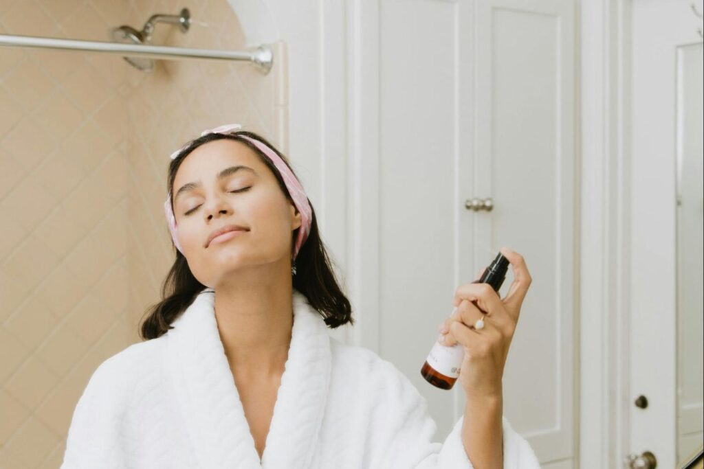 Woman spraying an acne scar treatment to her face in front of the mirror