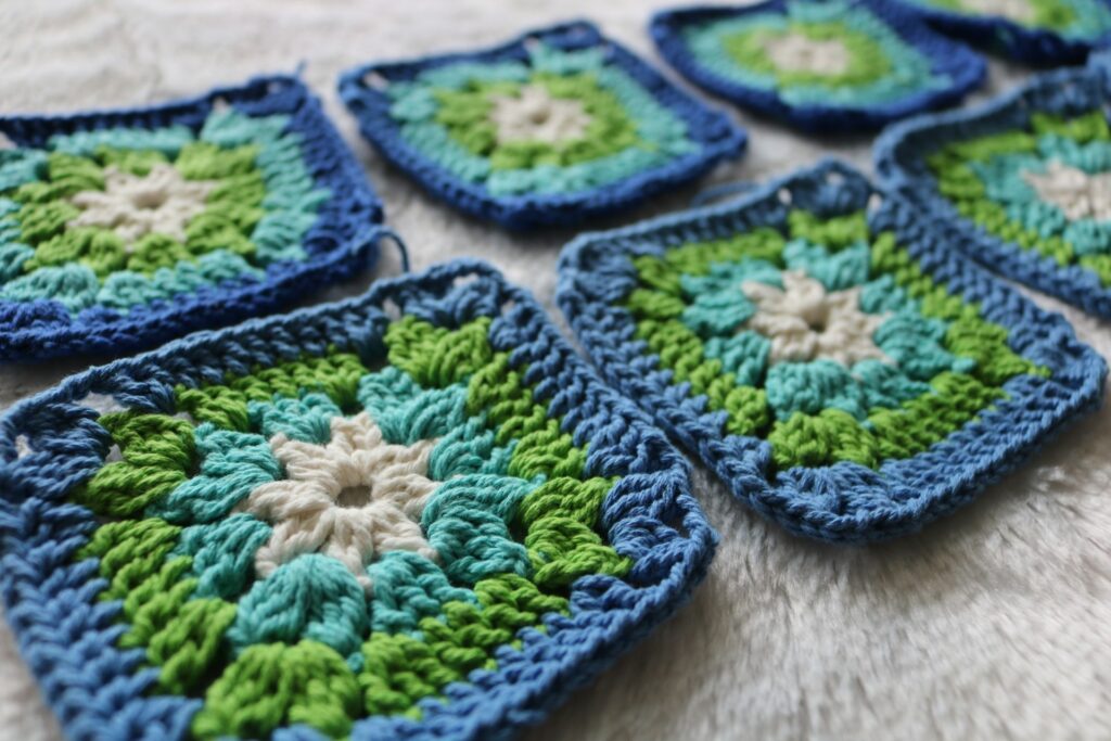 Crochet granny squares in blue, green and white are arranged on a white rug. The vivid colors create a cozy and artistic pattern.