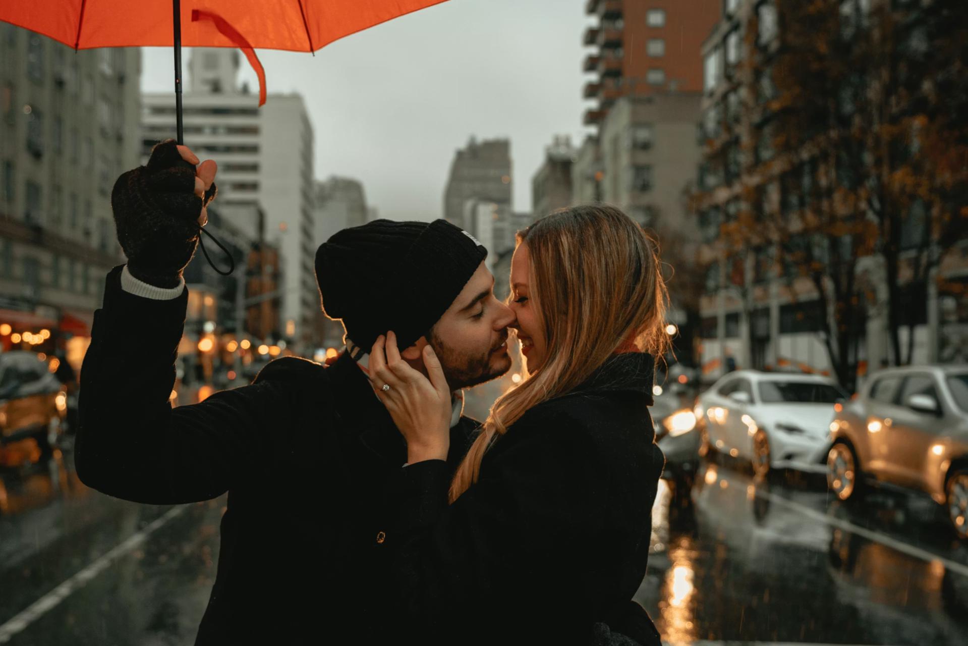 man and woman kissing in street under umbrella