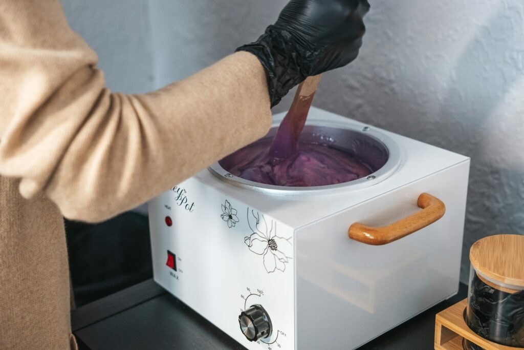 A beautician dipping a stick into a hot wax pot