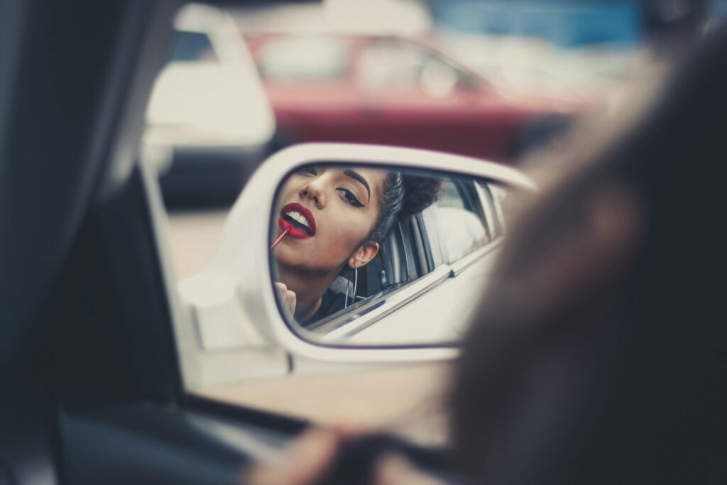 a woman applying red lipstick while in the car