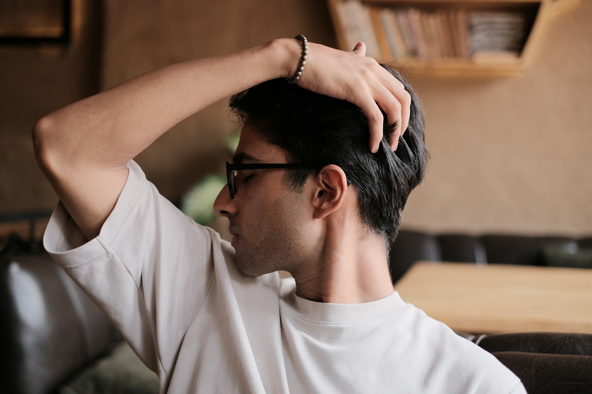 A man in a white shirt and black glasses, scratching his scalp