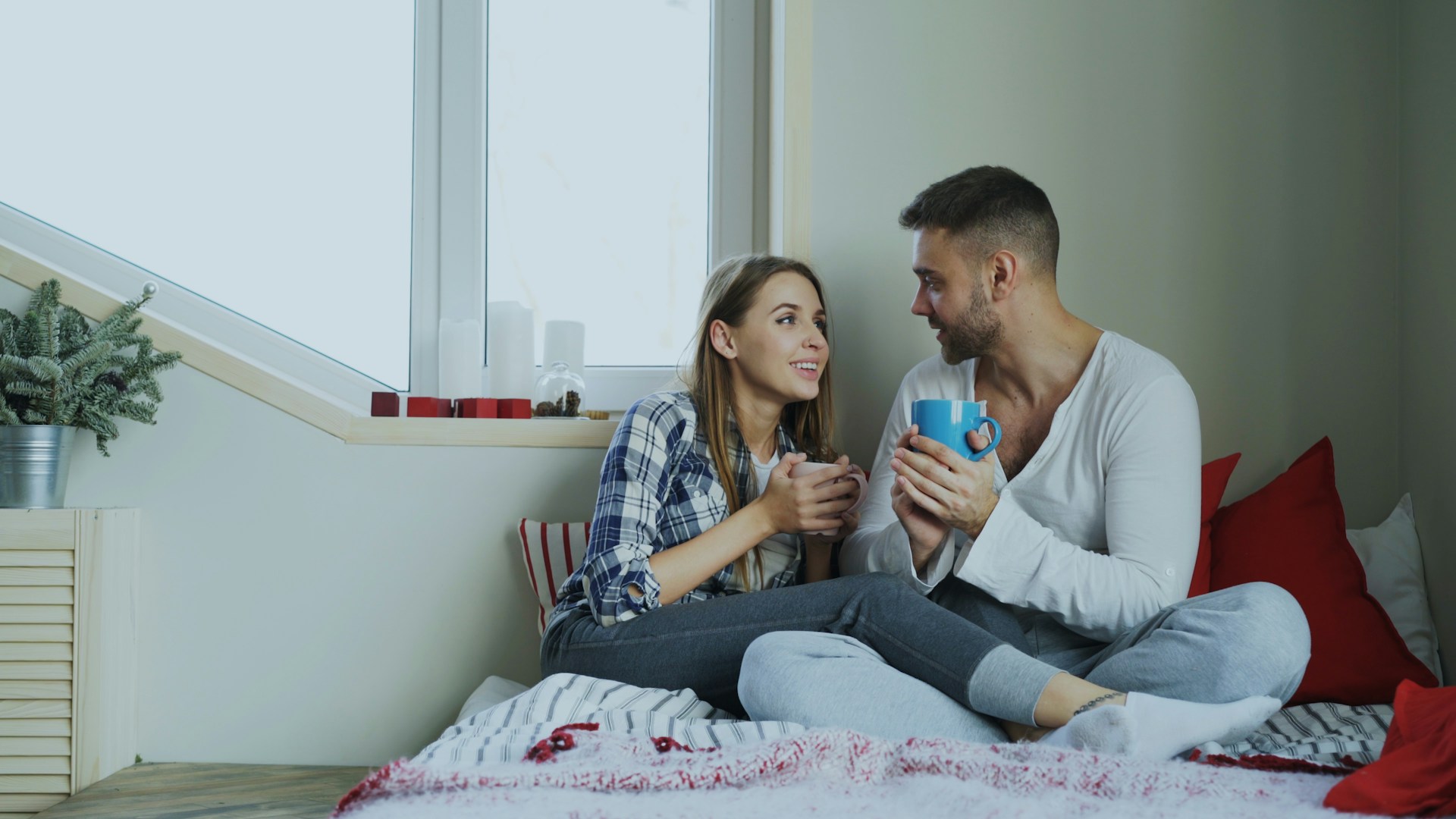 Man and woman talking in bed holding mugs