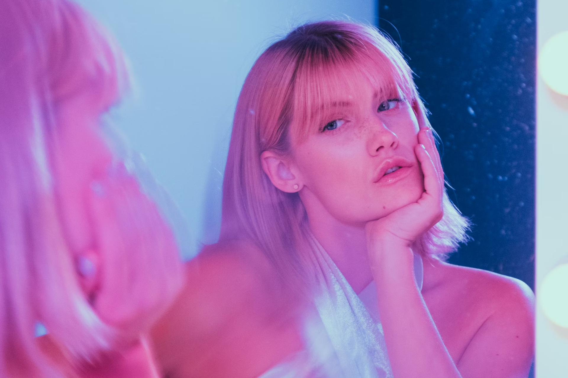 Blonde woman with pink glow looking in mirror